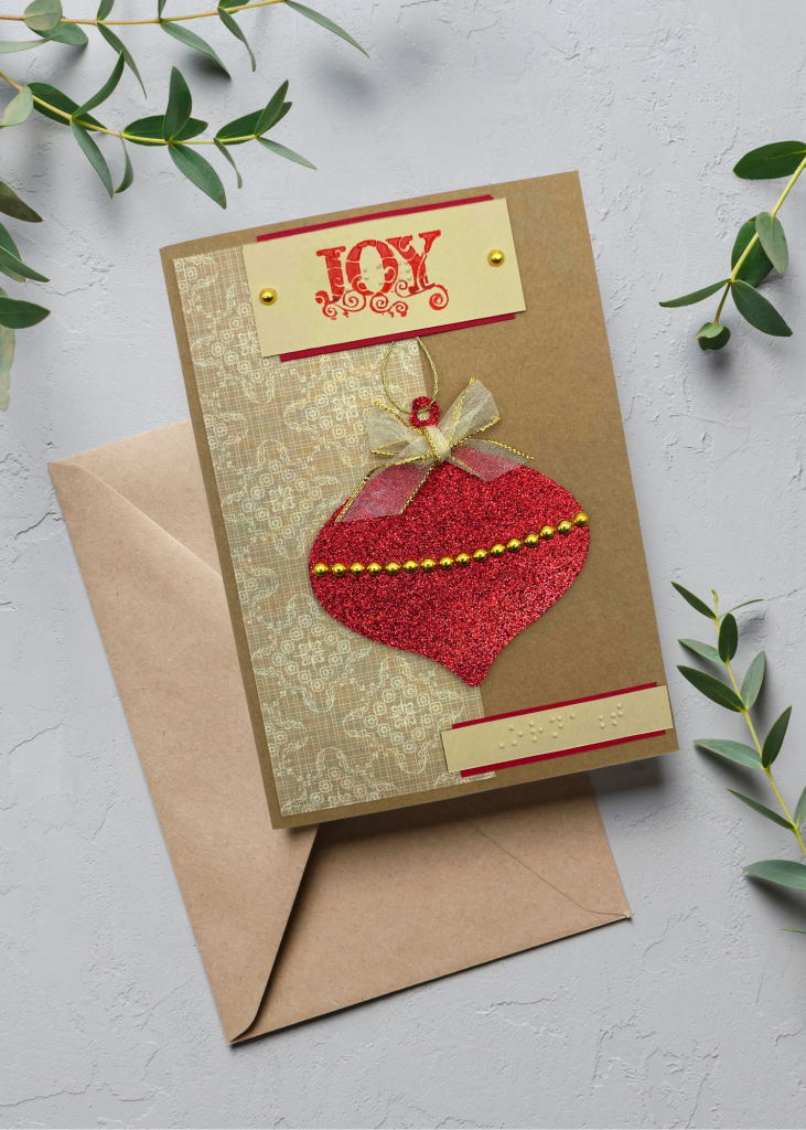the joy card sitting wit a brown envelope on a neutral grey backdrop