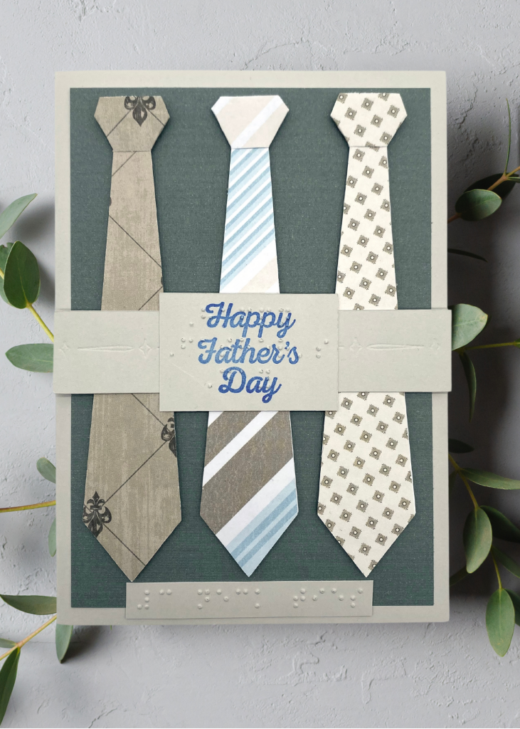 a pale grey card with 3 patterned neck ties which says Happy Father's day. The card is sitting on a neutral grey backdrop
