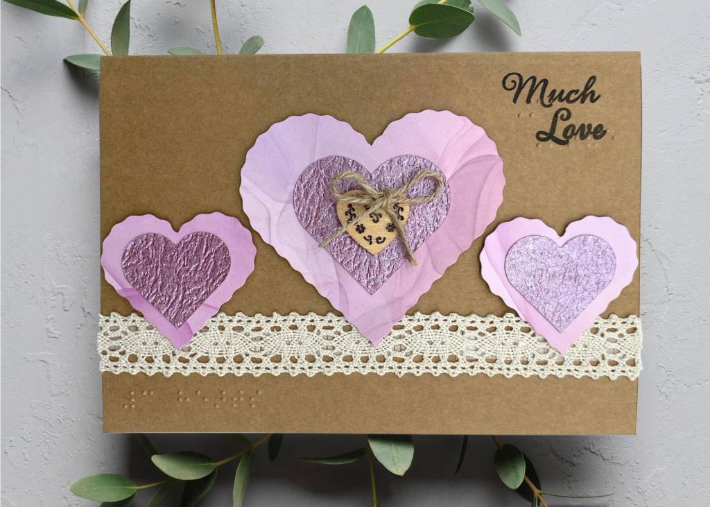 a light brown card with 3 nesting hearts which says Much Love. The card is sitting on a neutral grey backdrop