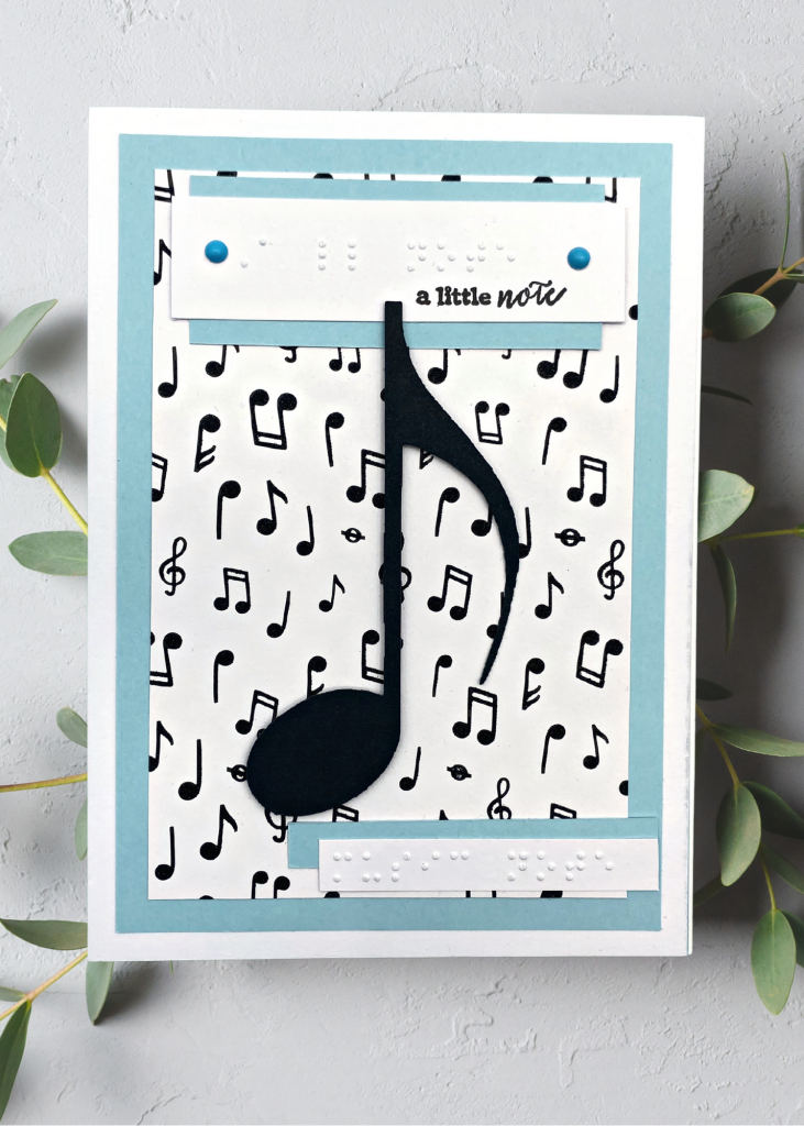 a blue and white card that says a little note with a big black eighth note sitting on a neutral grey backdrop