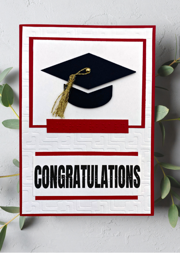 A White and red card that says Congratulations with a black graduation cap wit gold tassel on a neutral grey background.