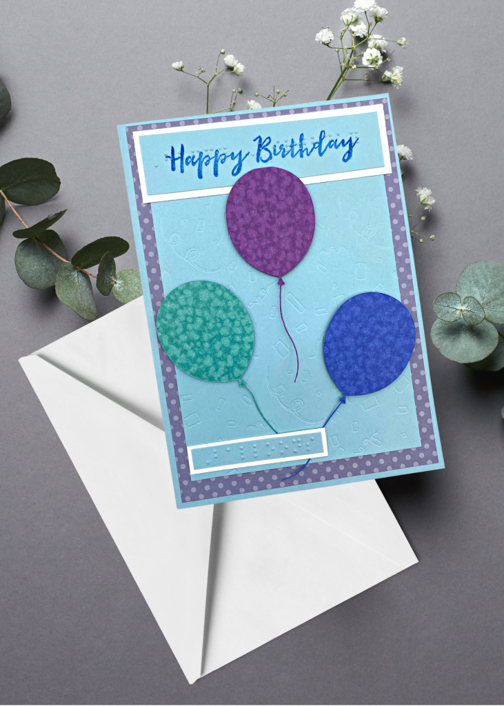 the happy birthday card sits with a white envelope on a neutral grey backdrop