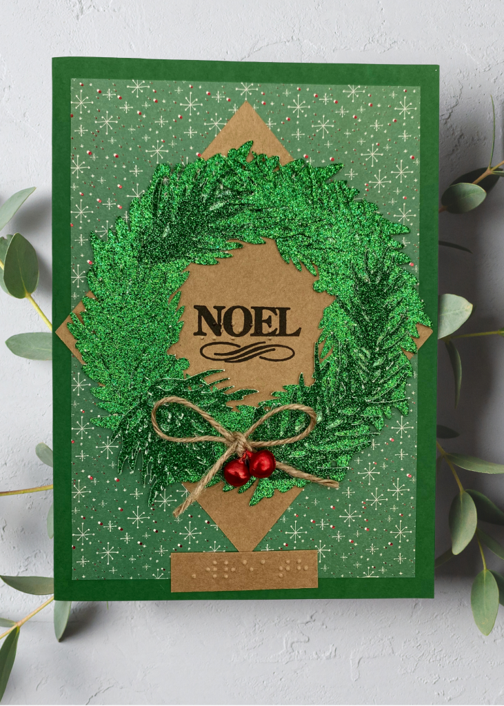 A vibrant green card with an evergreen wreath that says Noel on a neutral background